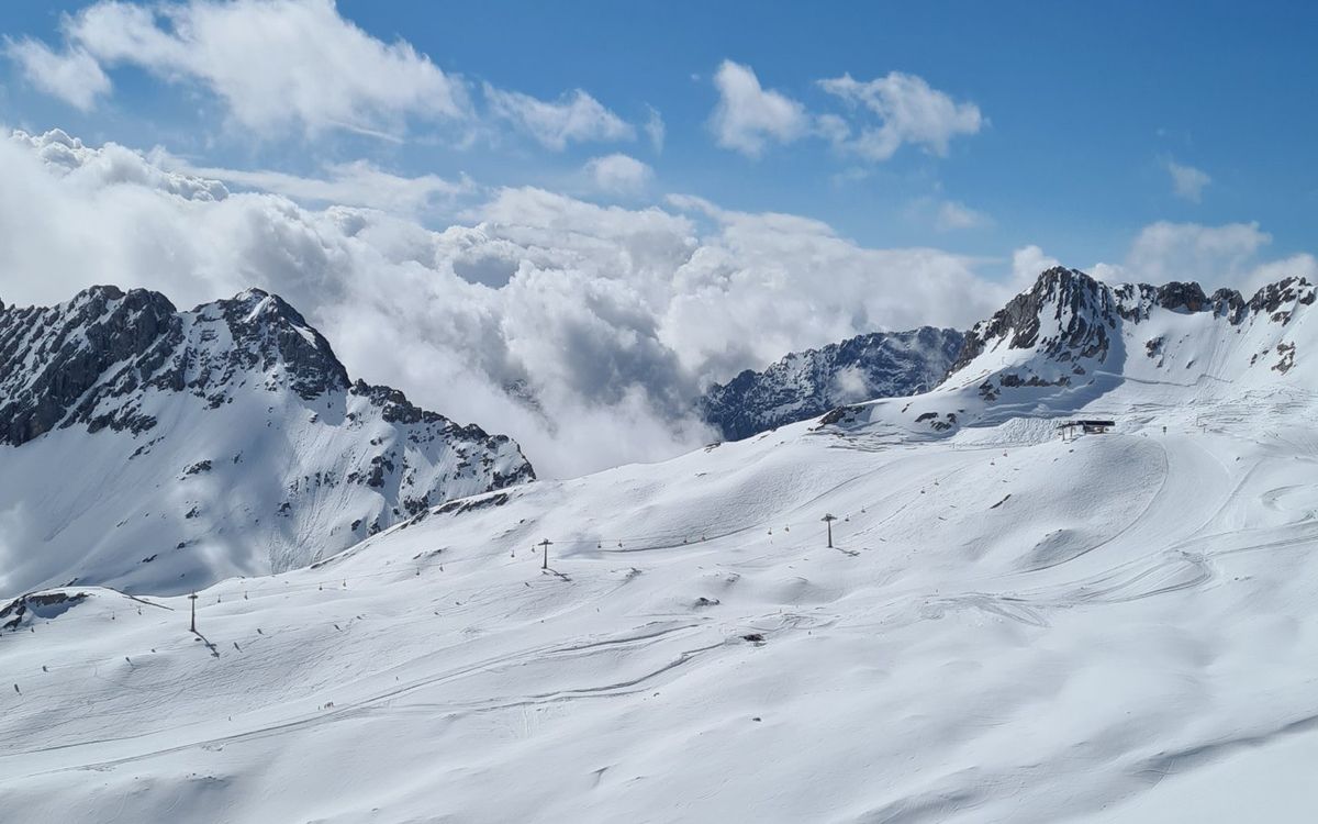 Weite Pistenhänge auf dem Zugspitzplatt vor Wolken und Felsgipfeln